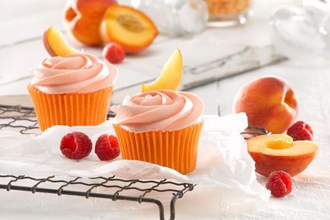 Cupcakes with peach coloured frosting surrounded by fresh peaches and raspberries