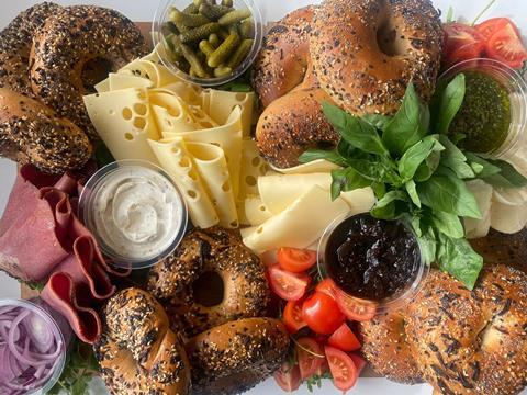 A board with seeded bagels, Swiss cheese, cornichons, pastrami and herbs on