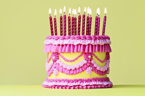 A pink and yellow birthday cake with intricate piped frosting and lots of candles on top