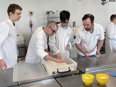 Students in white jackets looking at bread dough
