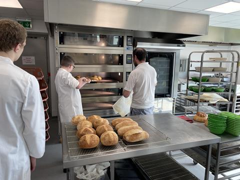 A student putting bread into the oven, being observed by a teacher