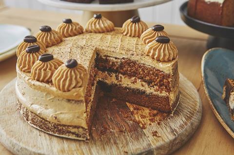 A coffee and walnut cake on a cake stand, with a slice taken out of it