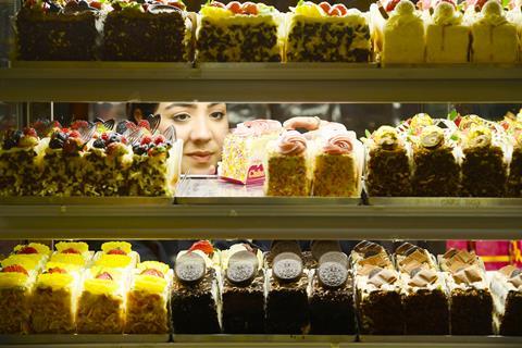 A lady takes a cake from a display shelf at a Cake Box store.