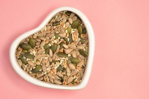 Seeds in a heart shaped bowl on a pink background