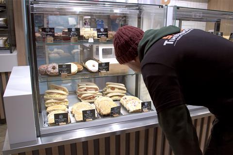 A person in a black hoodie and red beanie looking at baked goods in a display unit