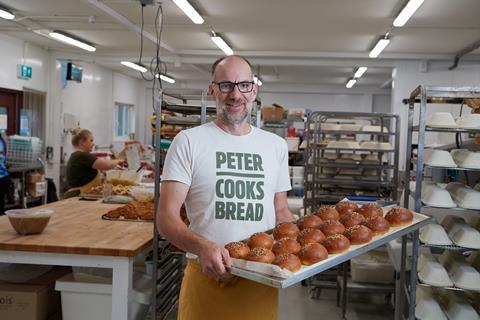 Peter Doughty-Cook in a bakery holding a tray of bread rolls