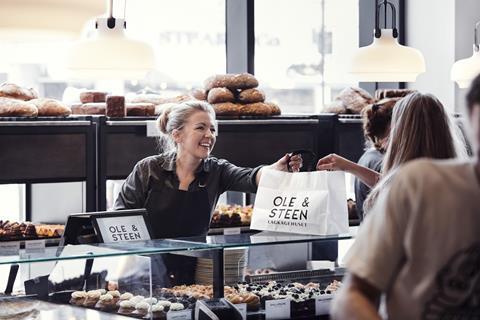 An employee at an Ole & Steen outlet passing a customer a bag of bakery items. 