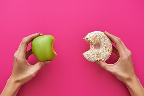 An apple and sprinkle covered doughnut on a pink background
