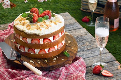 A layered strawberry and cream cake with strawberries on top and a glass of pink fizz next to it