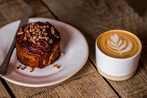 A chocolate & hazelnut bun on a white plate next to a latte
