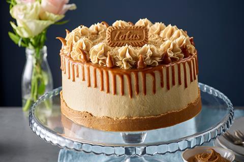 A Lotus Biscoff cake with caramel drip and Lotus Biscoff cream on a glass cake stand