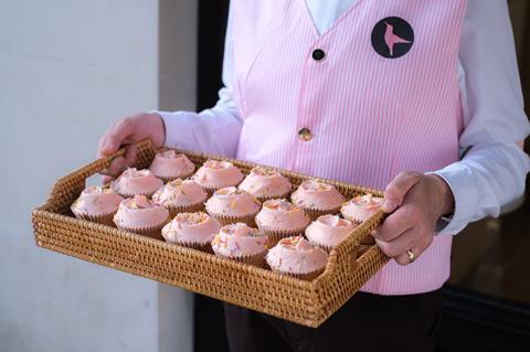 Pink cupcakes in a basket being held by a man in a pink waistcoat