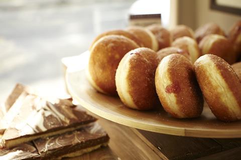 A circle of sugared jam doughnuts on a wooden cake stand