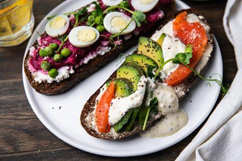 Two smorrebrods (Danish open sandwiches) with different toppings : salmon, avocado, cream cheese and quail eggs, beetroot paste, green pea on slice of rye bread