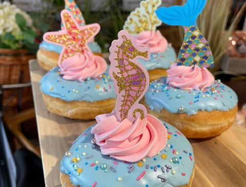 A selection of doughnuts with blue icing, sprinkles and cardboard mermaid decorations on top