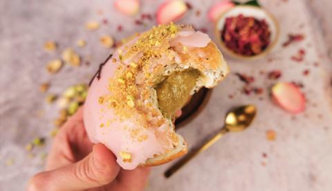 A pistachio & rose doughnut with a bite taken out of it and pistachio filling oozing out