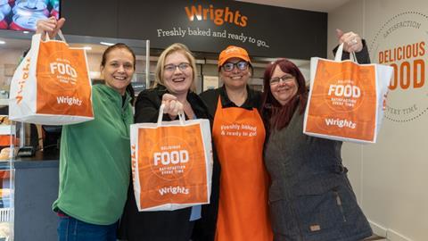 Four women holding orange bags in front of a Wrights bakery