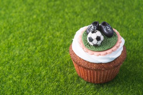 A vanilla cupcake with edible football and football boots on top