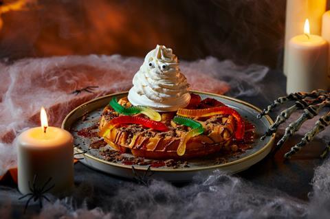 A waffle with cream ghost and gummy worms on top, with fake spiderwebs all around